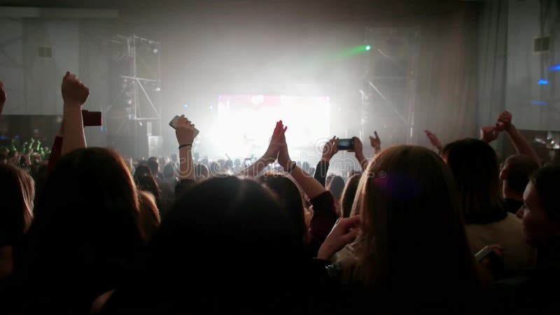 Fans auf Livekonzert, Menge von den Leuten belichtet durch die bunten Lichter, klatschend mit den Händen oben