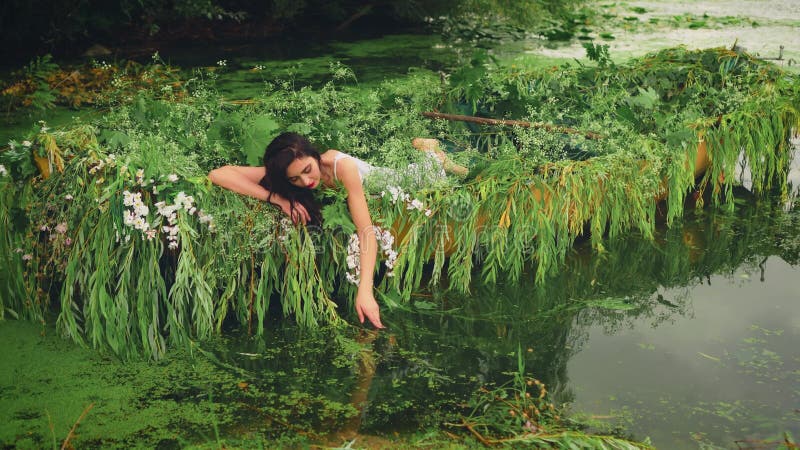 Fantasy szczęśliwa brunetka kobieta leży w łodzi dotykając wody jej ręka. dziewczyna księżniczka