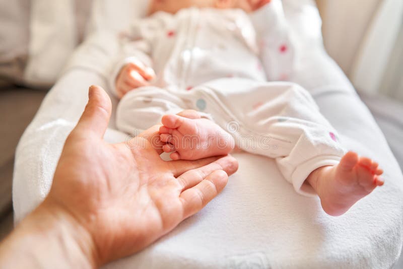 Far som håller i händerna fötter till det nyfödda barnet. babysmå fötter i föräldrarnas hand. fötter och hud. lycklig familj royaltyfri fotografi