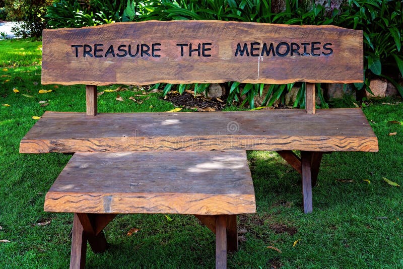 A timber bench under a tree with the words Treasure The Memories imprinted on the back. A timber bench under a tree with the words Treasure The Memories imprinted on the back