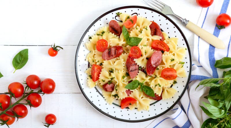 Farfalle saporito della pasta con le salsiccie arrostite, i pomodori ciliegia freschi ed il basilico su un piatto su un fondo di immagine stock Farfalle saporito della pasta con le salsiccie arrostite, i pomodori ciliegia freschi ed il basilico su un piatto su un fondo di immagine stock