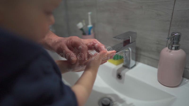 Farfar lär små morson att tvätta händer. Grabben tvättar händerna i badrummet över tvättmaskinen. handhygien