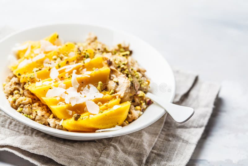 Farina d'avena con il mango, la noce di cocco, il burro di arachidi ed i dadi in un piatto bianco L'alimento del vegano, la prima immagini stock libere da diritti Farina d'avena con il mango, la noce di cocco, il burro di arachidi ed i dadi in un piatto bianco L'alimento del vegano, la prima immagini stock libere da diritti