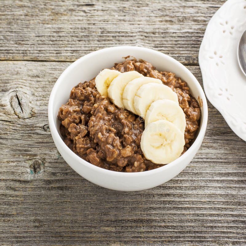 Farina d'avena del cioccolato per la prima colazione con le fette di banana matura e di pezzi di buon cioccolato amaro in una cio fotografia stock Farina d'avena del cioccolato per la prima colazione con le fette di banana matura e di pezzi di buon cioccolato amaro in una cio fotografia stock
