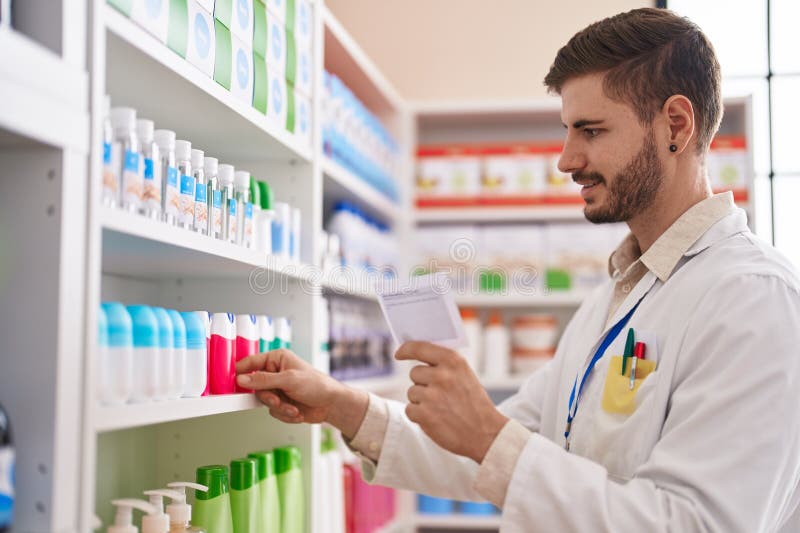 Farmacist caucazian tânăr care citește prescripții care conțin produse obținute din rafturi la farmacie royalty free stock photos