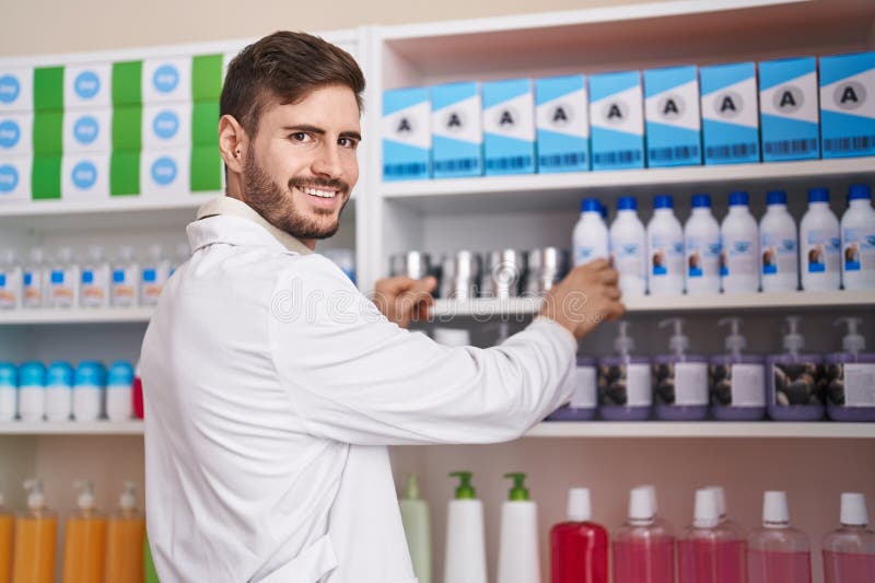 Farmaciștii tineri caucazieni zâmbind încrezători ținând un produs pe rafturi la farmacie stock photos