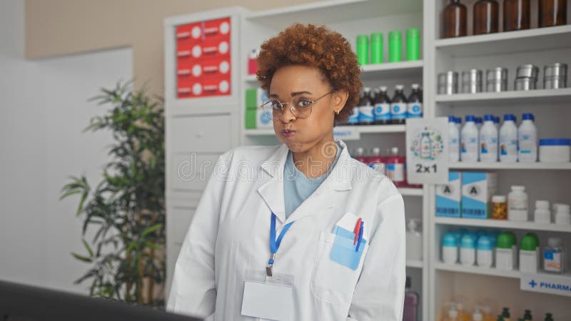 Farmacéutica afroamericana con abrigo blanco en el interior de una farmacia con estantes de medicamentos fotografía de archivo