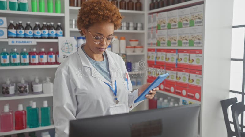 Farmacéutica afroamericana trabajando en una farmacia moderna navegando por una tableta fotos de archivo