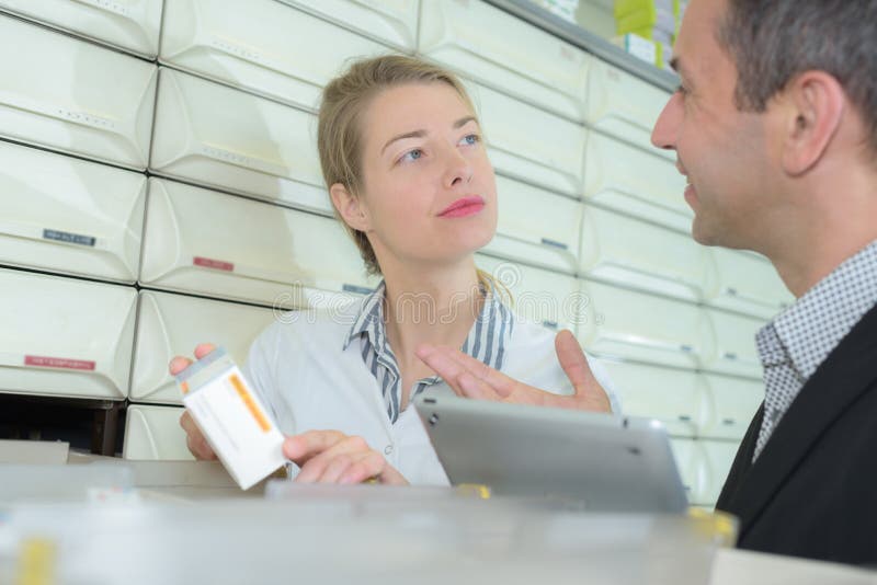 Farmacêutico experiente do gerente que aconselha o colega de trabalho fêmea na farmácia moderna fotos de stock Farmacêutico experiente do gerente que aconselha o colega de trabalho fêmea na farmácia moderna fotos de stock