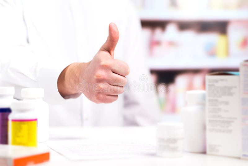 Farmacêutico feliz que mostra os polegares acima no contador da farmácia
