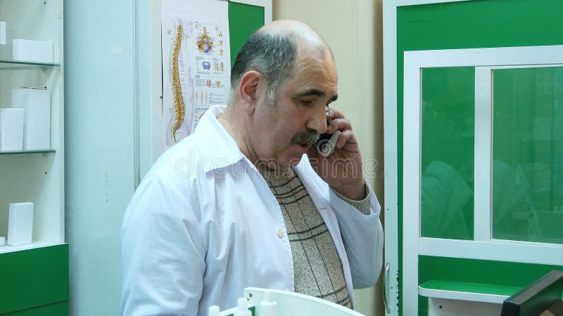 Farmacêutico superior que fala no telefone celular ao verificar a prescrição na farmácia fotos de stock Farmacêutico superior que fala no telefone celular ao verificar a prescrição na farmácia fotos de stock