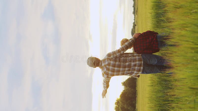 Farmer and his son in front of a sunset agricultural landscape. Man and a boy in a countryside field. Fatherhood stock video
