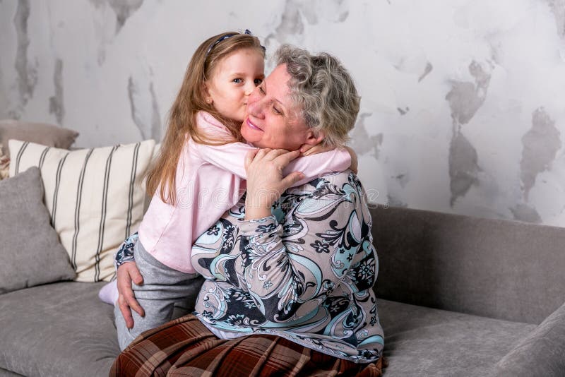 Farmodern och hennes lilla sondotter h?ller ?gonen p? filmer tillsammans och spelar p? apparaten, medan sitta p? soffan royaltyfria bilder Farmodern och hennes lilla sondotter h?ller ?gonen p? filmer tillsammans och spelar p? apparaten, medan sitta p? soffan royaltyfria bilder
