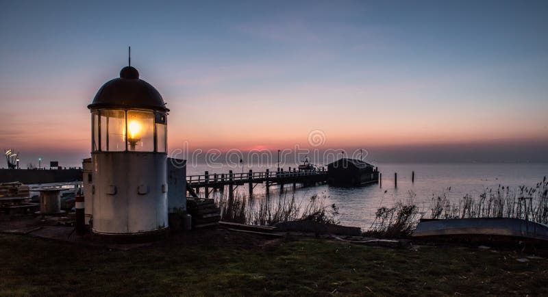 Farol da cabeça de Heceta próximo à doca de madeira ao lado do mar durante o pôr do sol imagem de stock Farol da cabeça de Heceta próximo à doca de madeira ao lado do mar durante o pôr do sol imagem de stock