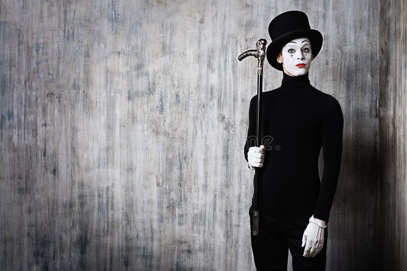 Elegant expressive male mime artist posing with walking stick by a grunge wall. Elegant expressive male mime artist posing with walking stick by a grunge wall.