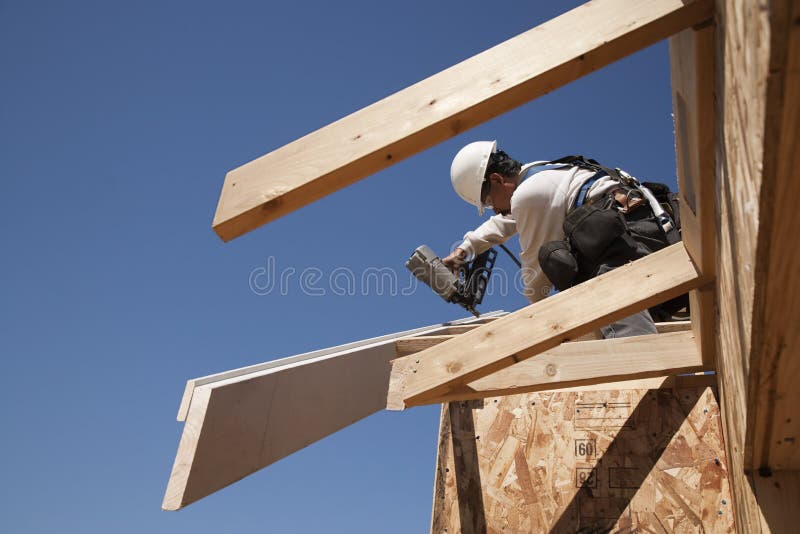 Low angle view of male workman or roofer fastening wooden beams on unfinished rooftop. Low angle view of male workman or roofer fastening wooden beams on unfinished rooftop.