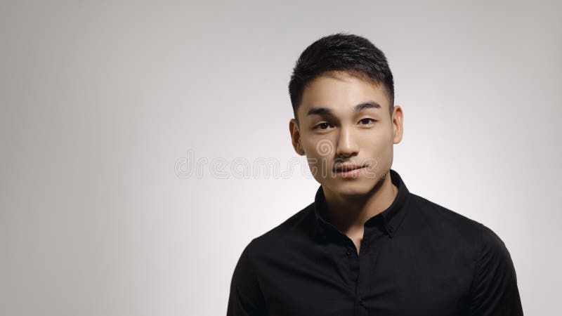 Close-up portrait of a handsome Asian man with short haircut posing in black shirt against gray background in the studio. Indoor photo of a happy guy in stylish black clothing looking at camera. Close-up portrait of a handsome Asian man with short haircut posing in black shirt against gray background in the studio. Indoor photo of a happy guy in stylish black clothing looking at camera