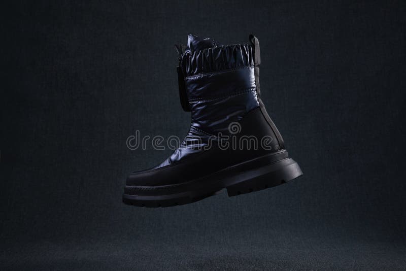 Fashion black unbranded boot flying on dark background. Black winter walking shoes levitate in air