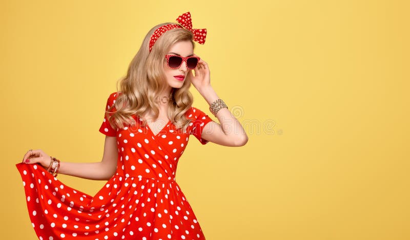 Fashion Model Girl in Polka Dots Summer Dress. Stylish Curly hairstyle, Trendy Clutch, fashion Red Headband, Sunglasses. Beauty Blond Pinup Woman in fashion pose. Glamour Playful Lady on Yellow. Fashion Model Girl in Polka Dots Summer Dress. Stylish Curly hairstyle, Trendy Clutch, fashion Red Headband, Sunglasses. Beauty Blond Pinup Woman in fashion pose. Glamour Playful Lady on Yellow
