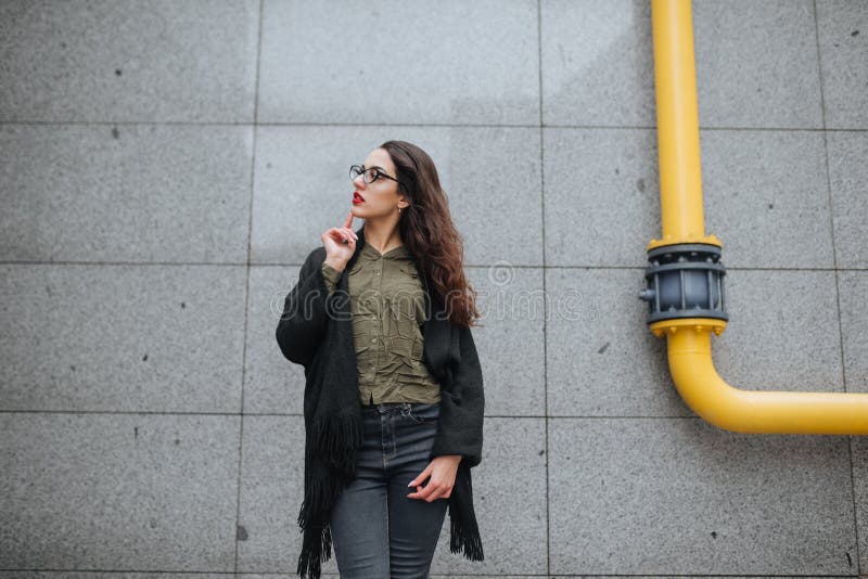 Fashion consept: beatiful young girl with long hair, glasses, red lips standing near modern wall wearing in green suit and grey je royalty free stock photo Fashion consept: beatiful young girl with long hair, glasses, red lips standing near modern wall wearing in green suit and grey je royalty free stock photo
