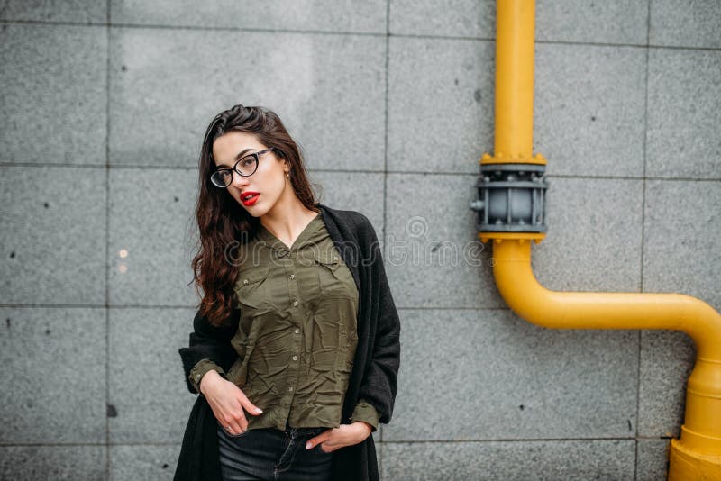 Fashion consept: beatiful young girl with long hair, glasses, red lips standing near modern wall wearing in green suit and grey je royalty free stock photo Fashion consept: beatiful young girl with long hair, glasses, red lips standing near modern wall wearing in green suit and grey je royalty free stock photo