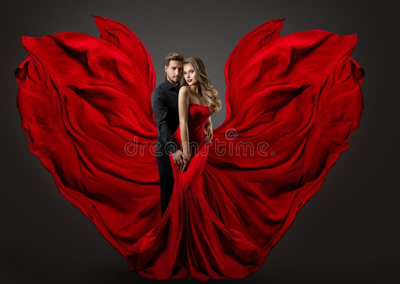 Fashion Couple in Love. Woman in fantasy long Red Gown and handsome Man. Flying Silk Fabric as Wings. Studio Portrait