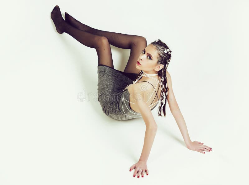 Fashion girl or pretty woman, fashionable model with stylish long, hair, braids, makeup. Sitting in grey dress and black, nylon pantyhose on white background. Fashion, underwear and hosiery