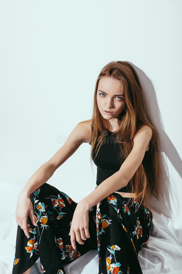 Fashion girl sitting on floor against white wall background.