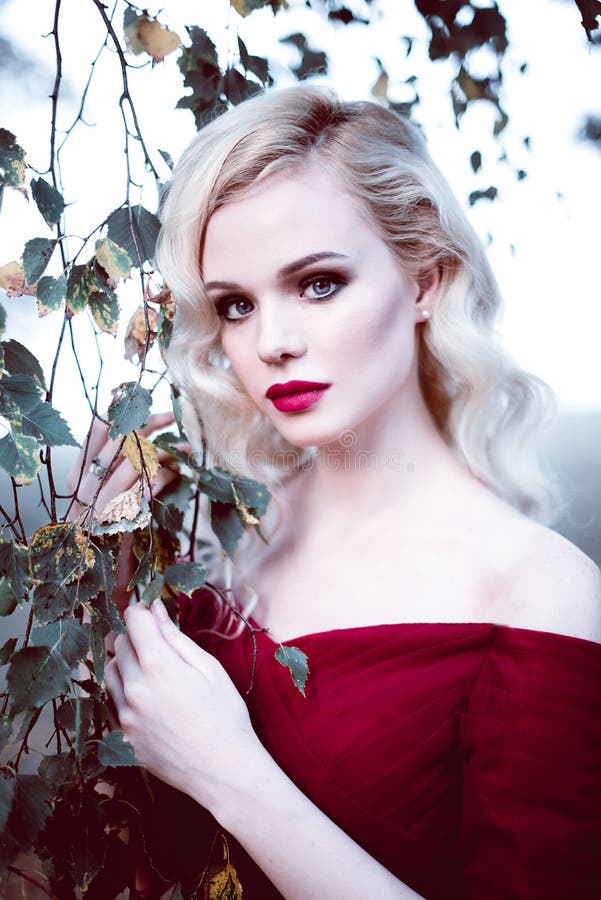 Fashion gorgeous young blonde woman in beautiful red dress in a fairy-tale forest. magic atmosphere. Retouched toning shot