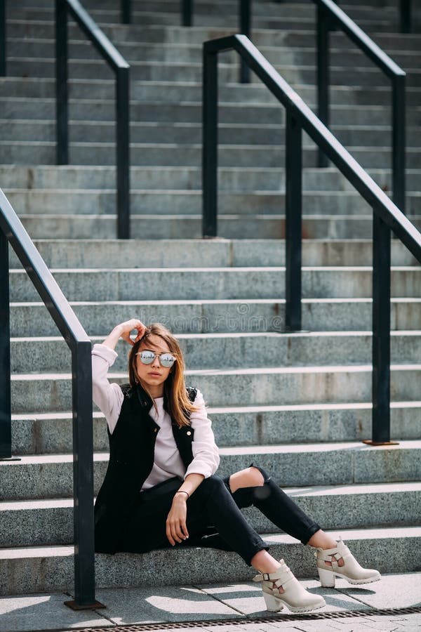 Fashion hipster cool girl in sunglasses. .urban background,fashion look. Model sitting on the stairs