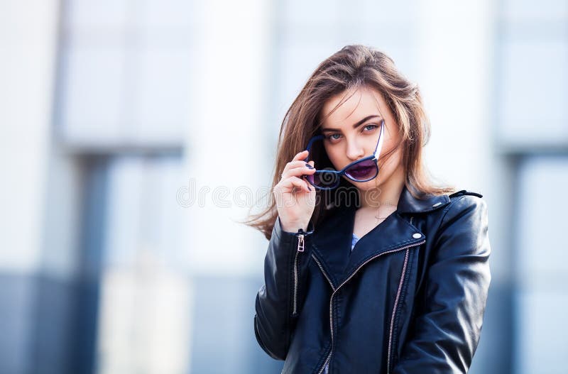 Fashion hipster woman posing outdoor. leather jacket,brunette hair, bright red lips, sunglasses.Street fashion concept.