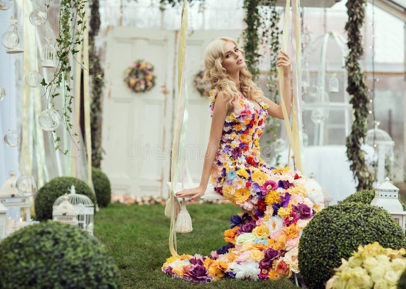 Fashion lady in spring scenery wearing flower dress and posing on swing