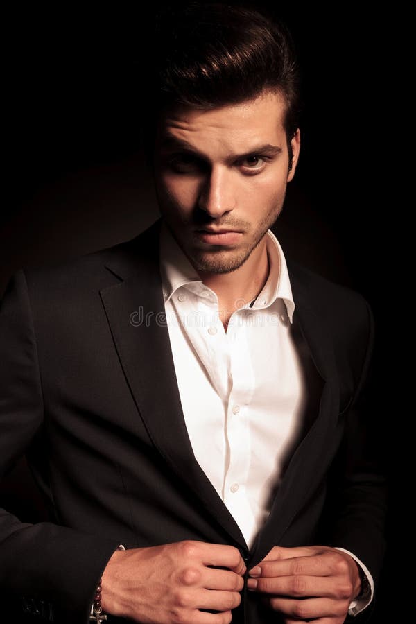 Portrait of a young fashion man buttoning his suit on black studio background. Portrait of a young fashion man buttoning his suit on black studio background