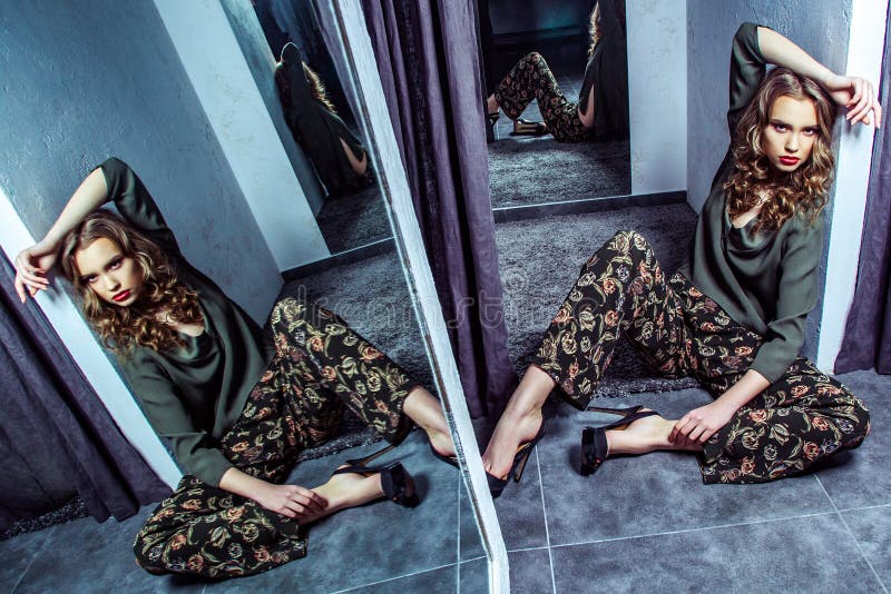 Fashion model with makeup and wavy hairstyle in stylish clothes and high heels shoes sitting on floor in fitting room and looking. At camera with serious face stock photography Fashion model with makeup and wavy hairstyle in stylish clothes and high heels shoes sitting on floor in fitting room and looking. At camera with serious face stock photography