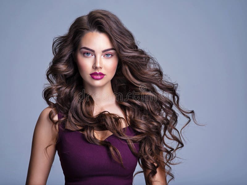 Face of a beautiful woman with long brown curly hair. Fashion model with wavy hairstyle. Attractive young  girl with curly hair