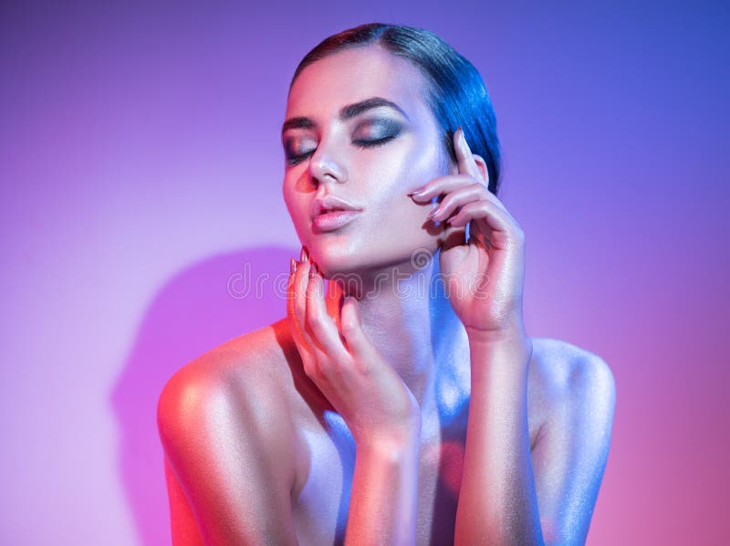 Fashion model woman in colourful bright sparkles and neon lights posing in studio, portrait of beautiful girl