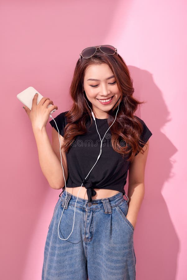 Fashion muchacha sonriente bastante genial, relajante, escuchando música con auriculares en un fondo rosa. imagen de archivo Fashion muchacha sonriente bastante genial, relajante, escuchando música con auriculares en un fondo rosa. imagen de archivo