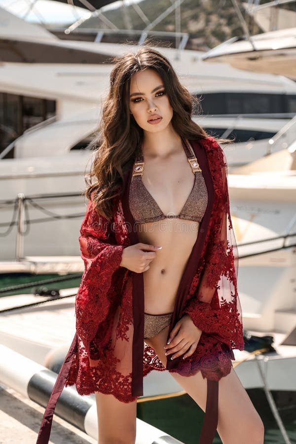 Woman with dark hair in elegant swimming suit posing near yachts