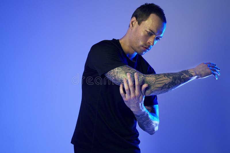 Fashion photoshoot of sport fit attractive man making arm stretch, tattooed hands, hipster look. Color flash studio light. royalty free stock photos Fashion photoshoot of sport fit attractive man making arm stretch, tattooed hands, hipster look. Color flash studio light. royalty free stock photos