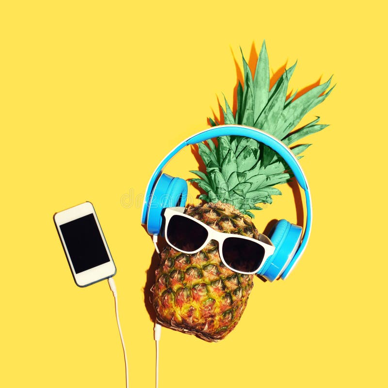 La moda di ananas con occhiali da sole e cuffie ascolta la musica su smartphone su sfondo giallo.