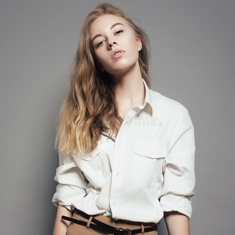 Fashion portrait of a beautiful young blonde woman in a white shirt in the studio on a gray background