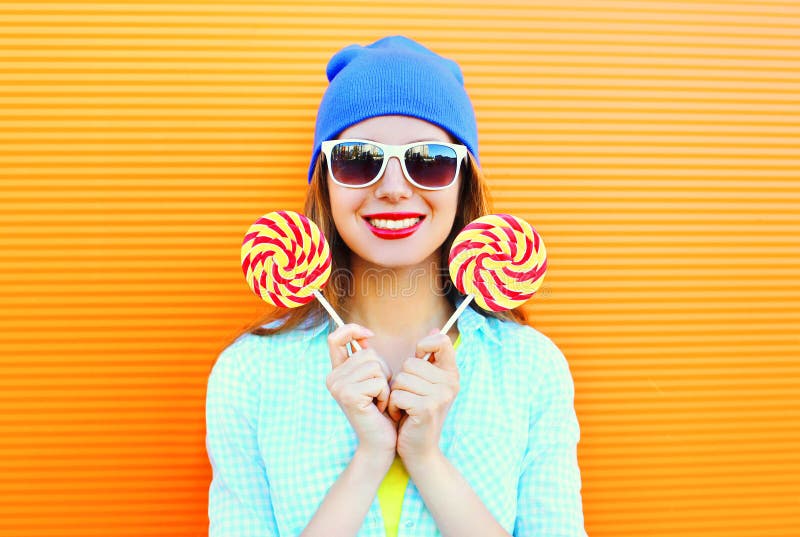Fashion portrait happy smiling young woman with a lollipop on stick over colorful orange