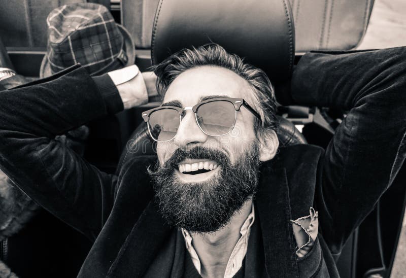 Fashion portrait of young bearded man ready for road trip - Cheerful hipster guy sitting in car looking the sky - Black and white