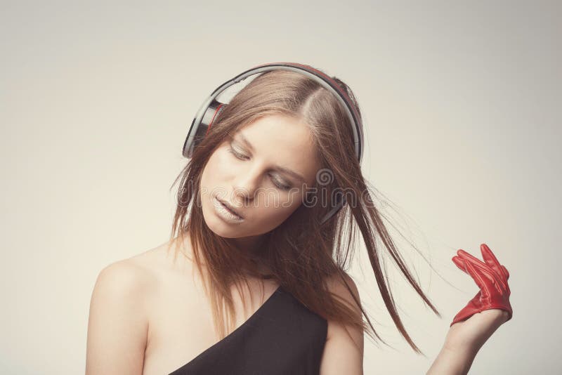 Fashion pretty girl listening music with headphones, wearing red gloves, close eyes and take pleasure with song