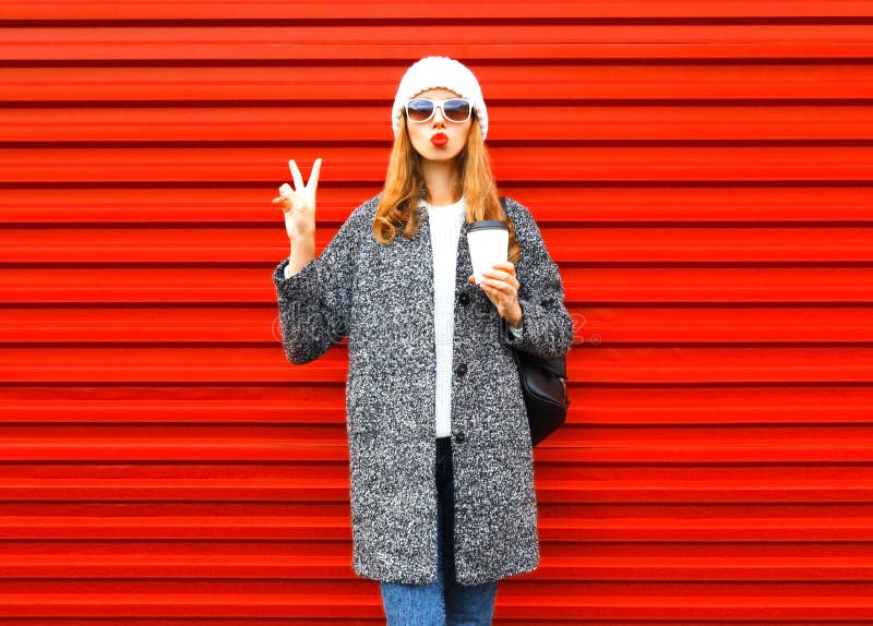 Moda bella donna con la tazza di caffè in cappotto in posa su sfondo rosso.