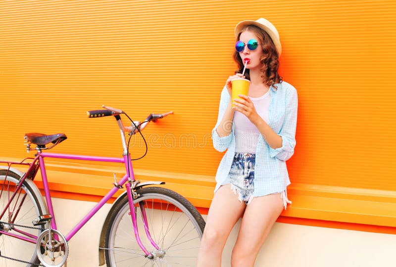 Fashion pretty woman drinks fruit juice from cup with retro bicycle over colorful orange royalty free stock photos Fashion pretty woman drinks fruit juice from cup with retro bicycle over colorful orange royalty free stock photos