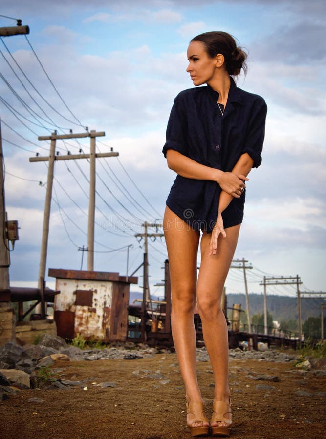 Fashion pretty young woman with long legs posing outdoor on the ground near a Electric poles. Beautiful brunette on heels only in royalty free stock image Fashion pretty young woman with long legs posing outdoor on the ground near a Electric poles. Beautiful brunette on heels only in royalty free stock image