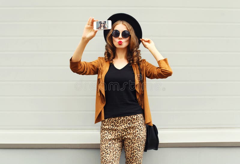 Fashion pretty young woman model taking photo picture self-portrait on smartphone wearing retro elegant hat, sunglasses