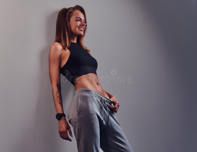 Fashion, sport, health. Slim fitness girl wearing sportswear leaning on a wall in a studio.