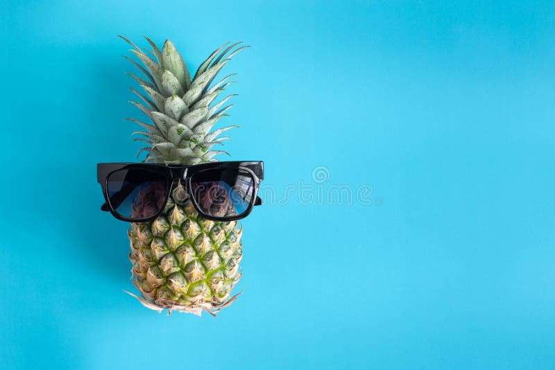 Fashion summer pineapple in black sunglasses on blue background . Pineapple for summer vacation and party concept